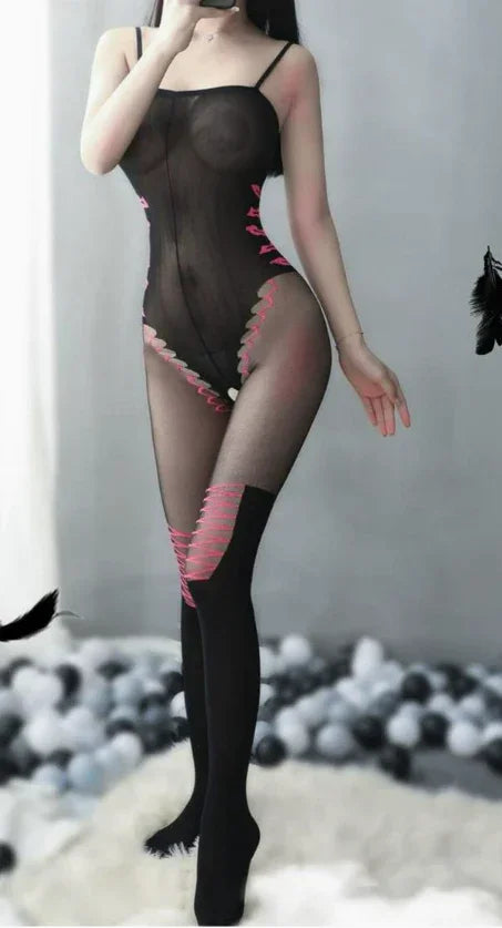 Woman wearing sheer black lace bodysuit with pink accents, standing in modern bedroom setting