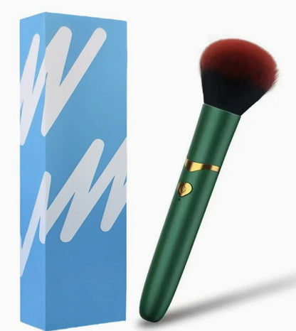 Green and gold makeup brush with fluffy red bristles beside a blue gift box